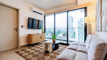 Uma sala de estar moderna com uma televisão de tela plana, um sofá, uma mesinha redonda e uma grande janela com vista para a cidade.