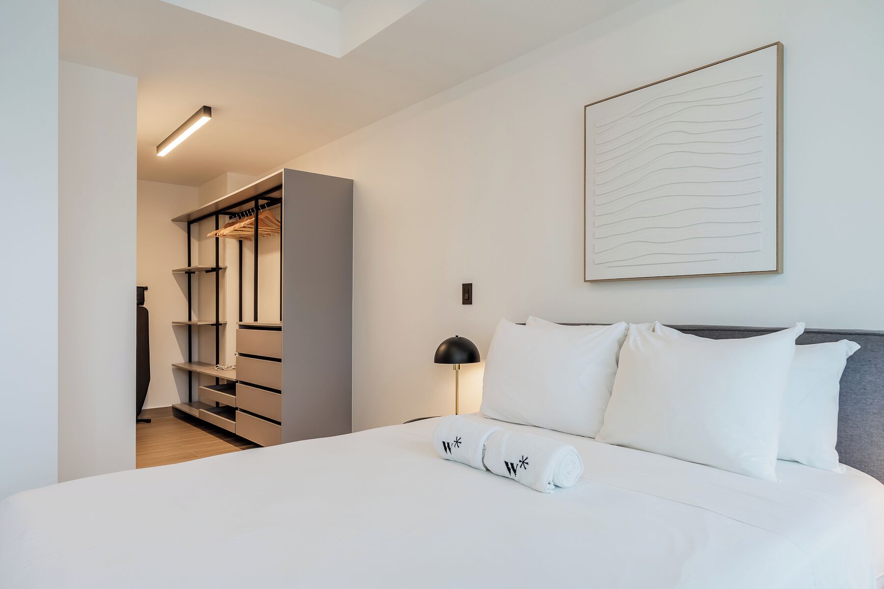 A hotel room with a bed, a nightstand, a lamp, a wardrobe, and a wall-mounted artwork.