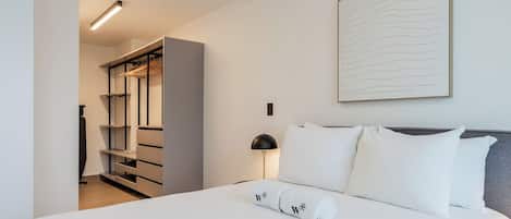 Una habitación de hotel con cama, mesita de noche, lámpara, armario y una obra de arte colgada en la pared.