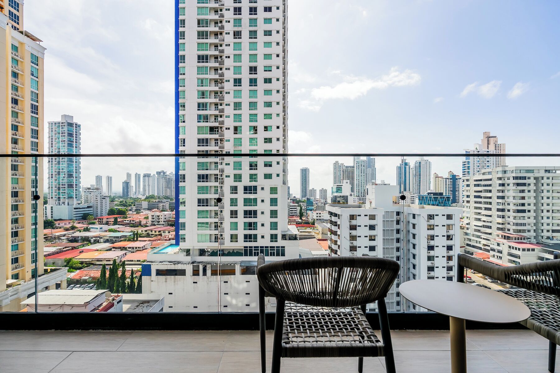 Un balcon offrant une vue sur le paysage urbain, avec des immeubles de grande hauteur et un ciel dégagé.