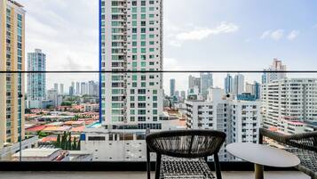 Un balcon offrant une vue sur le paysage urbain, avec des immeubles de grande hauteur et un ciel dégagé.