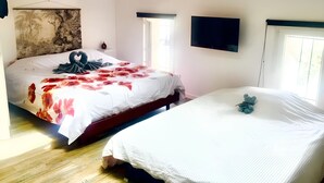 Une chambre avec deux lits, une poutre en bois au plafond, un téléviseur à écran plat et une fenêtre avec des stores.