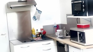 Une cuisine de taille réduite, équipée d’une cuisinière, d’un four à micro-ondes et de meubles de rangement blancs.