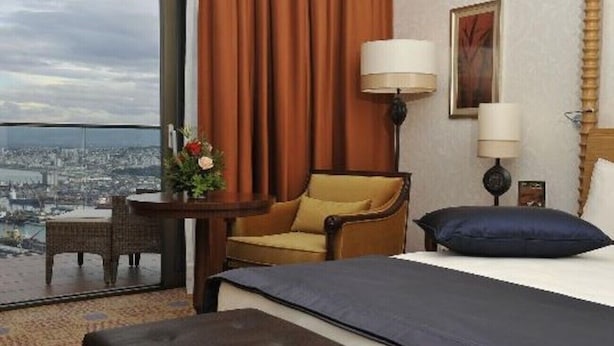 Habitación de hotel con cama, una silla, una mesa, una lámpara y vista a la ciudad.
