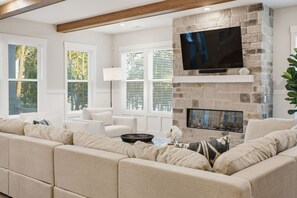 A living room with a stone fireplace, a flat-screen TV, and a beige sectional sofa. - Luxury New Build with Lake Norman Views & Resort Amenities- Sleeps 16 (Lake Norman of Catawba)