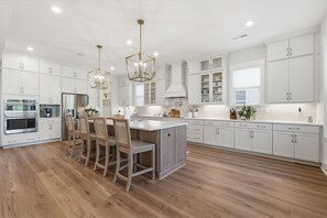 A modern kitchen with white cabinets, a central island with bar stools, stainless steel appliances, and pendant lighting. - Luxury New Build with Lake Norman Views & Resort Amenities- Sleeps 16 (Lake Norman of Catawba)