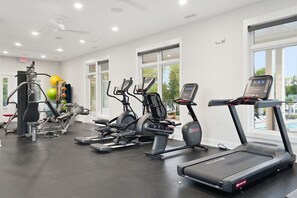 Une salle de sport équipée de divers appareils d’exercice, notamment des tapis de course, des vélos elliptiques et des stations d’entraînement en musculation.