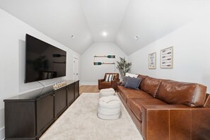 A modern living room with a flat-screen TV, dark wood entertainment unit, leather sofa, and a white rug. - Luxury New Build with Lake Norman Views & Resort Amenities- Sleeps 16 (Lake Norman of Catawba)
