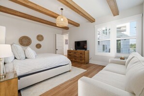 Ein modernes Schlafzimmer mit einem Bett, Nachttisch, Lampe und einem Fernseher auf einer Holzkommode.