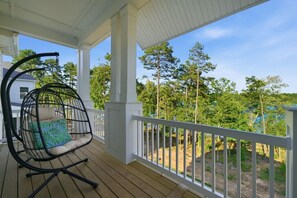 A covered porch with a swing chair and a view of trees. - Luxury New Build with Lake Norman Views & Resort Amenities- Sleeps 16 (Lake Norman of Catawba)