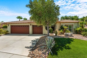 A two-story house with a garage, a well-maintained lawn, and a variety of desert plants. - Entire Home + Private Casita | Private Pool & Spa | Putting Green | Fully Fenced Yard| Community Amenities (Palm Springs)