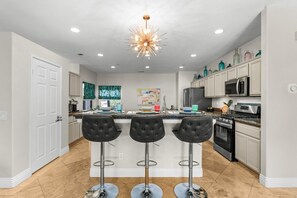 A modern kitchen with a central island, bar stools, stainless steel appliances, and decorative items on the shelves. - Entire Home + Private Casita | Private Pool & Spa | Putting Green | Fully Fenced Yard| Community Amenities (Palm Springs)