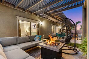 An outdoor living area with a fire feature, a cushioned seating area, and a pergola structure. - Entire Home + Private Casita | Private Pool & Spa | Putting Green | Fully Fenced Yard| Community Amenities (Palm Springs)