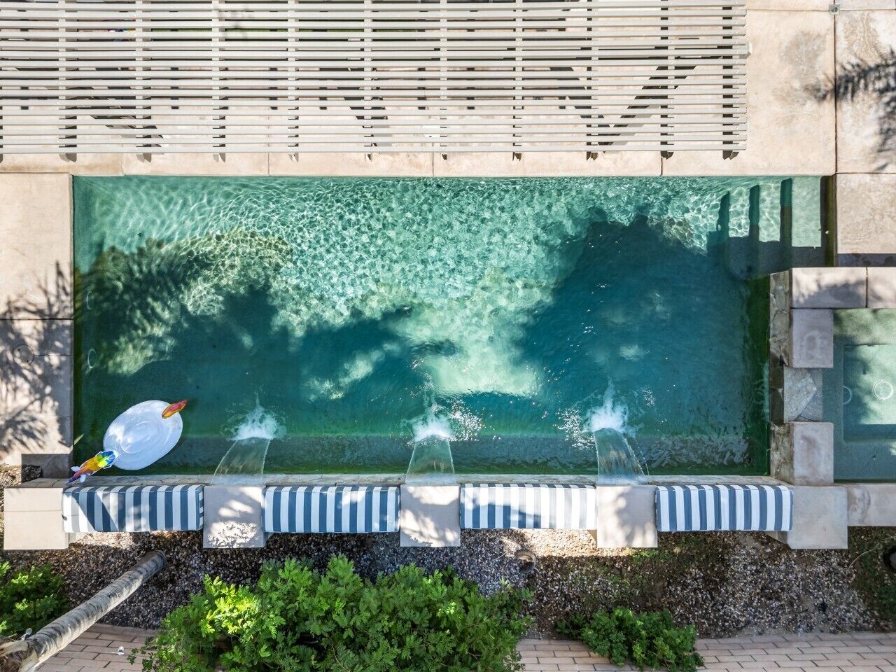 A swimming pool with clear water, a water feature, and a lounge area with striped cushions.
