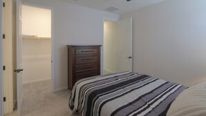 Ein Schlafzimmer mit einem Bett, einer Kommode, einem Deckenventilator und einer Tür zu einem anderen Raum.