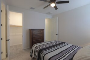 Quarto com cama, penteadeira, ventoinha no teto e porta para outro espaço.