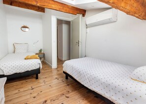 A bedroom with two beds, wooden flooring, a ceiling fan, and an air conditioning unit. - A charming 130-square-meter cottage in the heart of a village farmhouse (Entre Vignes)