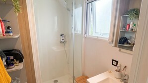 A bathroom with a glass-enclosed shower, a sink, a mirror, and a shelf with toiletries. - Homerez - Bungalow in Saint-Raphaël (Saint-Raphaël)