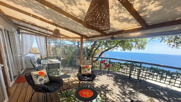 A covered outdoor deck with wooden flooring, a table, chairs, and a hanging light fixture. - Homerez - Bungalow in Saint-Raphaël (Saint-Raphaël)
