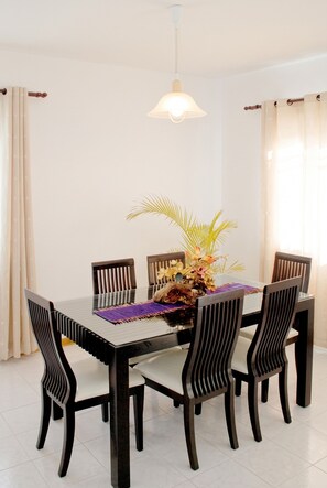 A dining area with a rectangular table, six chairs, a hanging light fixture, and a decorative centerpiece.