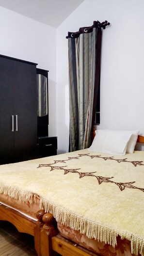 A bedroom with a bed, a wardrobe, a nightstand, and a curtain.