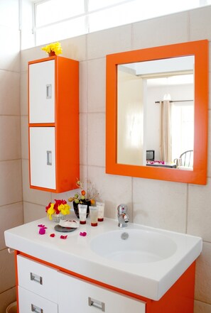 A bathroom with a white sink, orange cabinet, and mirror.