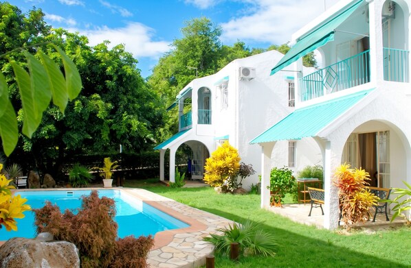 A white building with a swimming pool, surrounded by lush greenery and a clear sky.