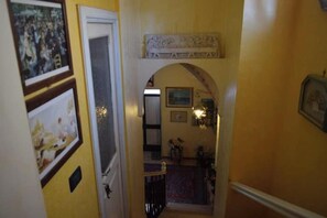 Un corridoio stretto con una porta a sinistra, un arco decorativo al centro e una piccola scala che conduce a un livello superiore.