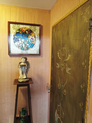 Una stanza con una porta in legno decorata, una finestra a vetri colorati sopra una statua e un tavolino con una lanterna verde.
