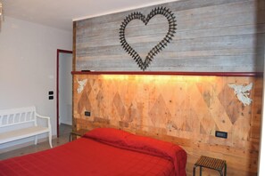 Ein Schlafzimmer mit einem Holzkopfteil, einer herzförmigen Dekoration, einer weißen Bank und einer roten Bettdecke.