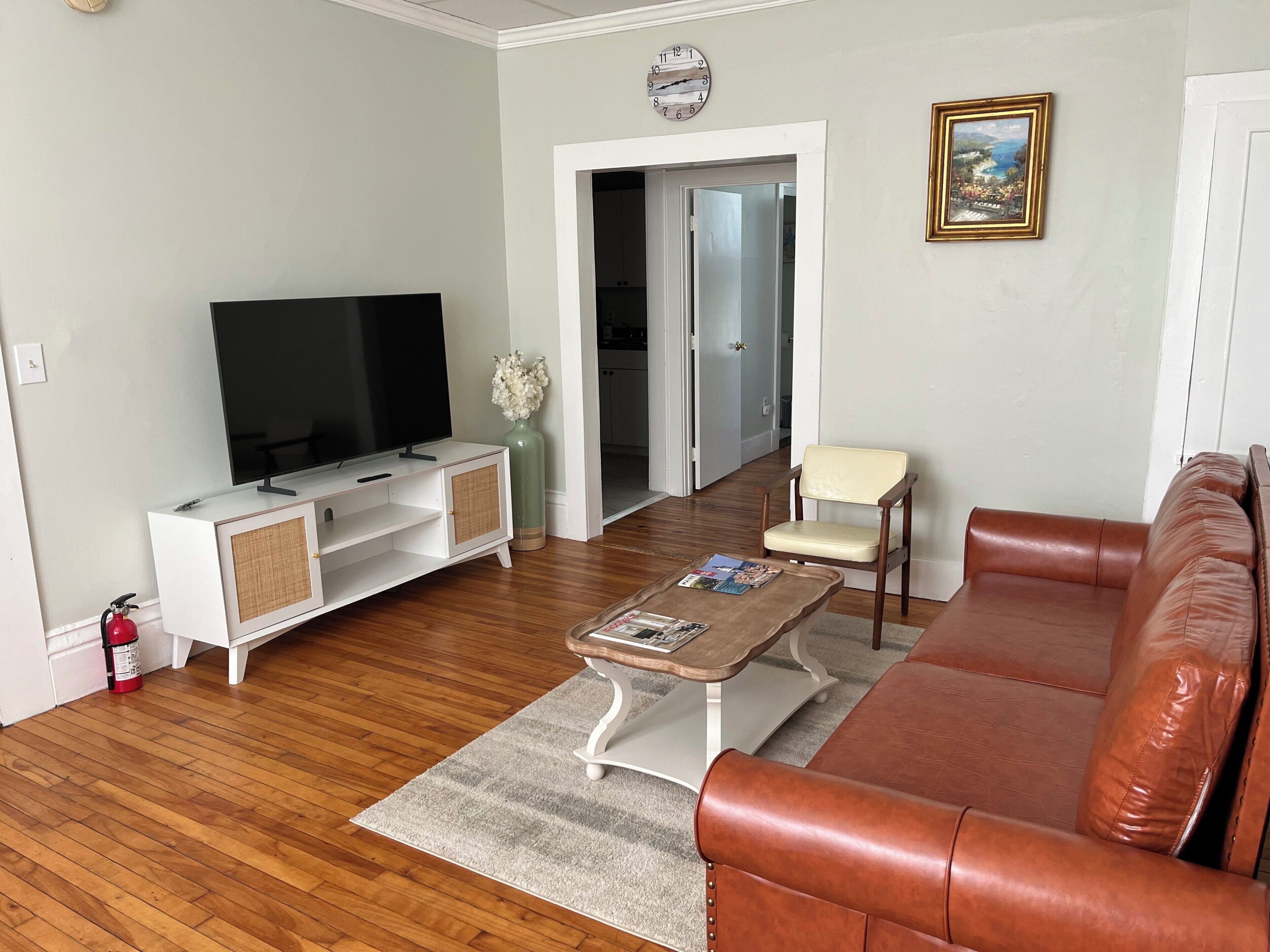 A living room with a television, a sofa, a coffee table, and a door leading to another room.