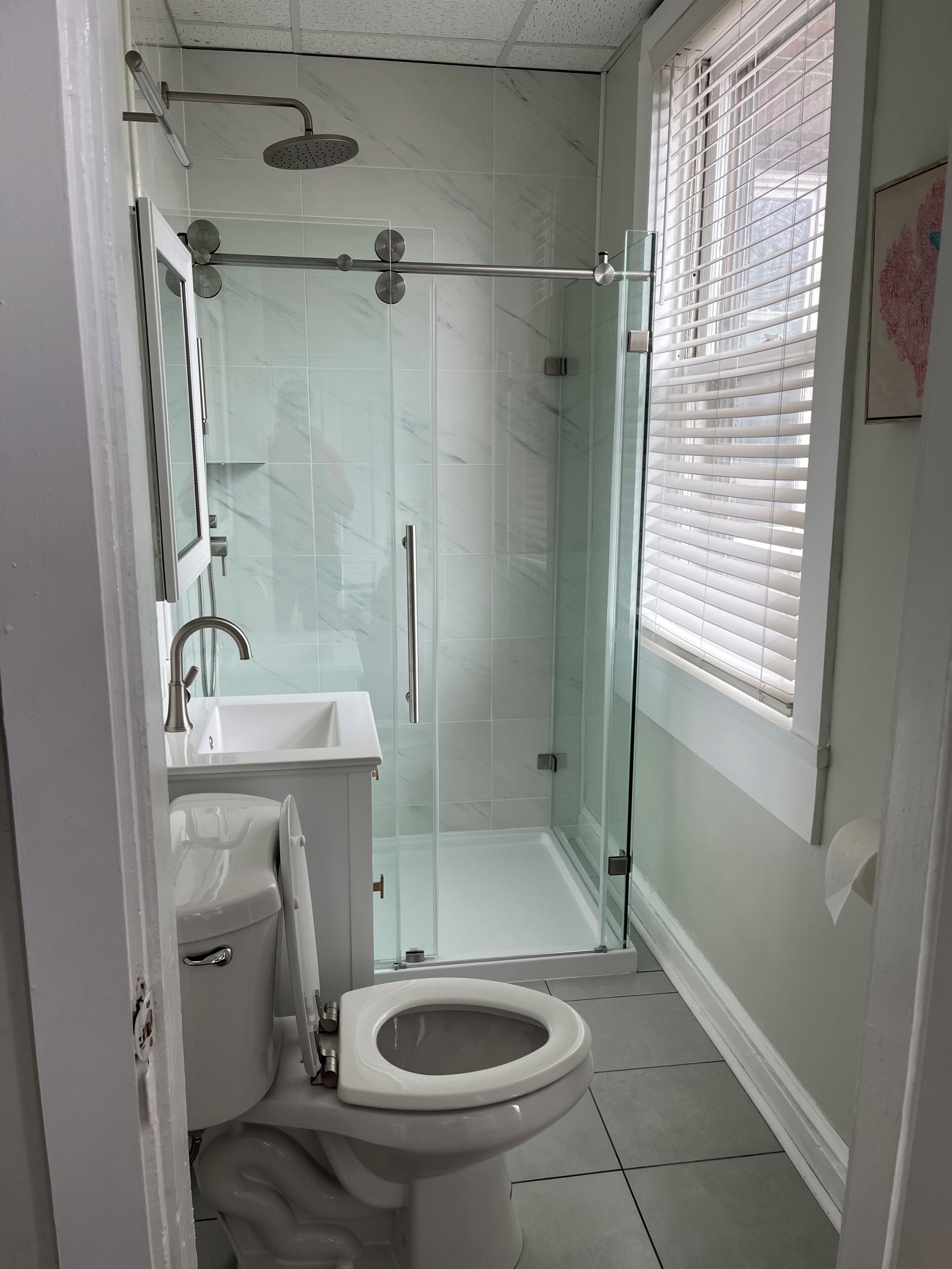 A modern bathroom with a glass-enclosed shower, a toilet, and a sink.