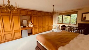 Ein Schlafzimmer mit einem großen Bett, einem Holzschrank, einem Schreibtisch mit Stuhl, einer Kommode und einer Deckenleuchte.