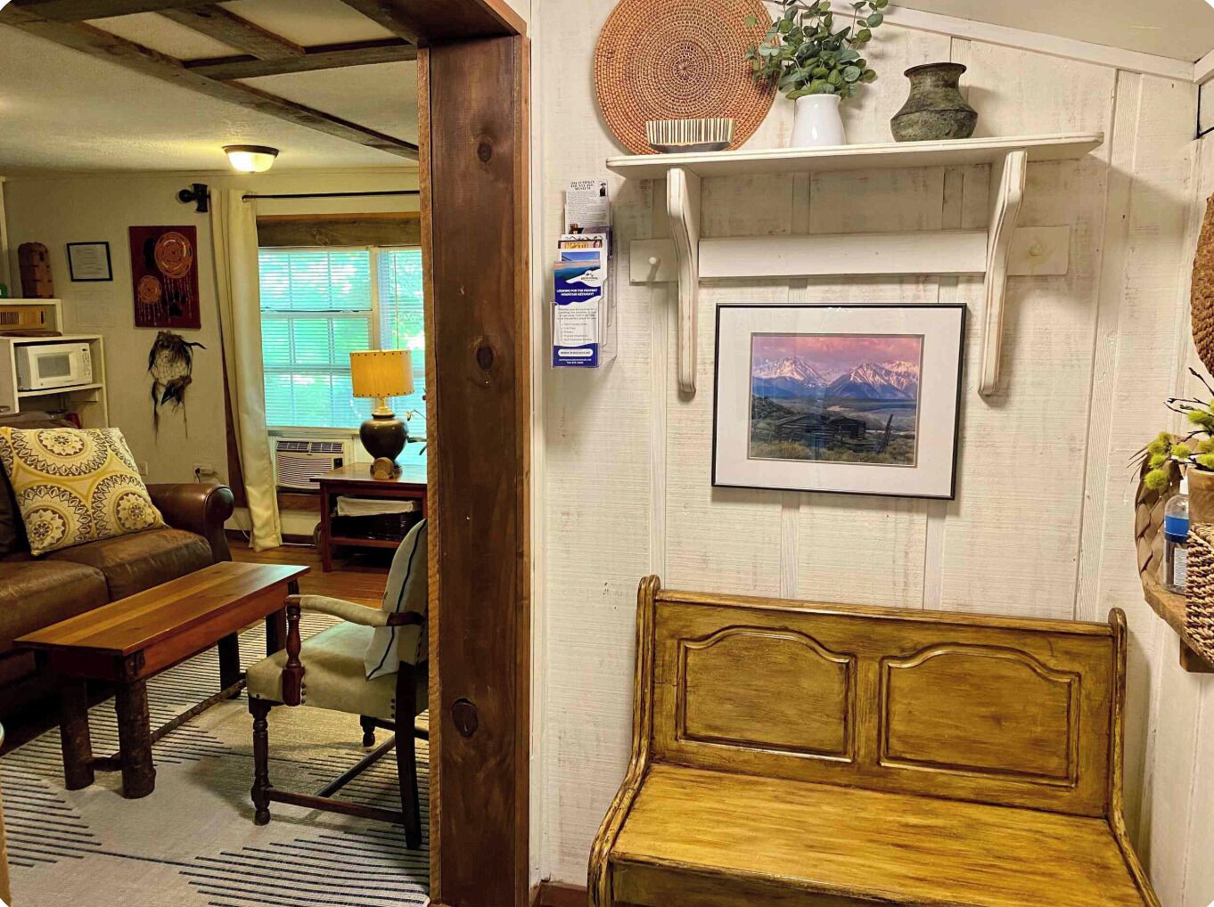 Un salon chaleureux avec un banc en bois, un canapé et une table à manger. Un meuble mural est fixé au mur, orné d’objets décoratifs et d’un tableau encadré.