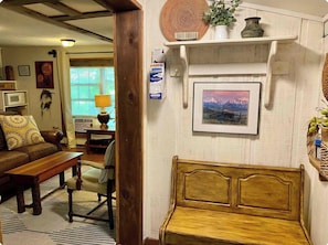 A cozy living room with a wooden bench, a sofa, and a dining table. There is a wall-mounted shelf with decorative items and a framed picture. - Two Cottages in the Woods! 4 mins to Dahlonega Square (Dahlonega)