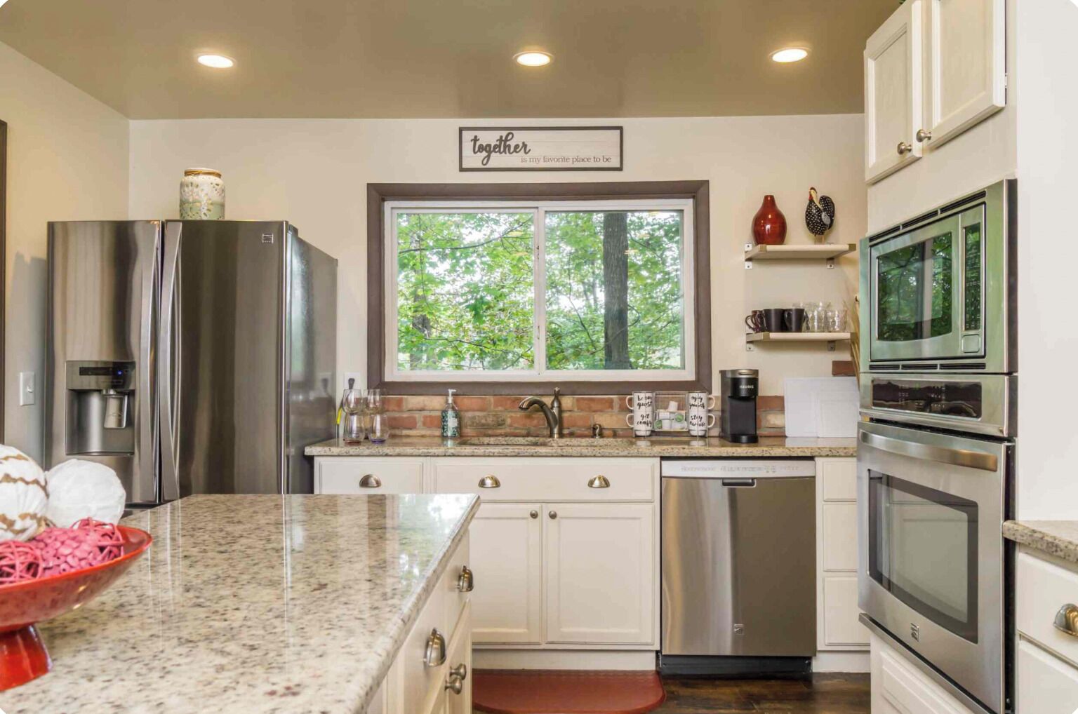 Una cocina moderna con electrodomésticos de acero inoxidable, encimera de granito y ventana con vista a árboles.