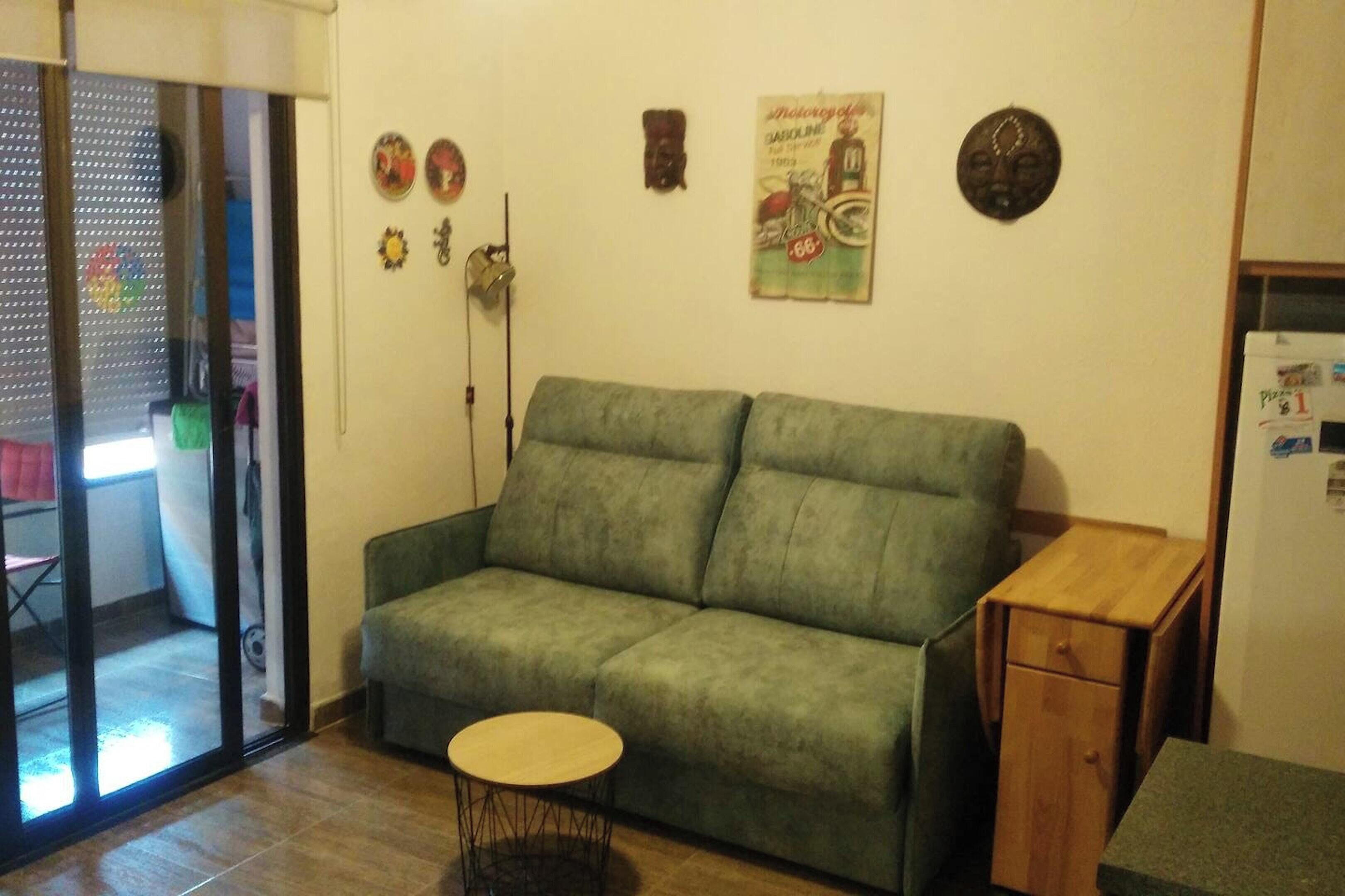 A green sofa, a small round table, and a wooden cabinet in a room with a tiled floor.