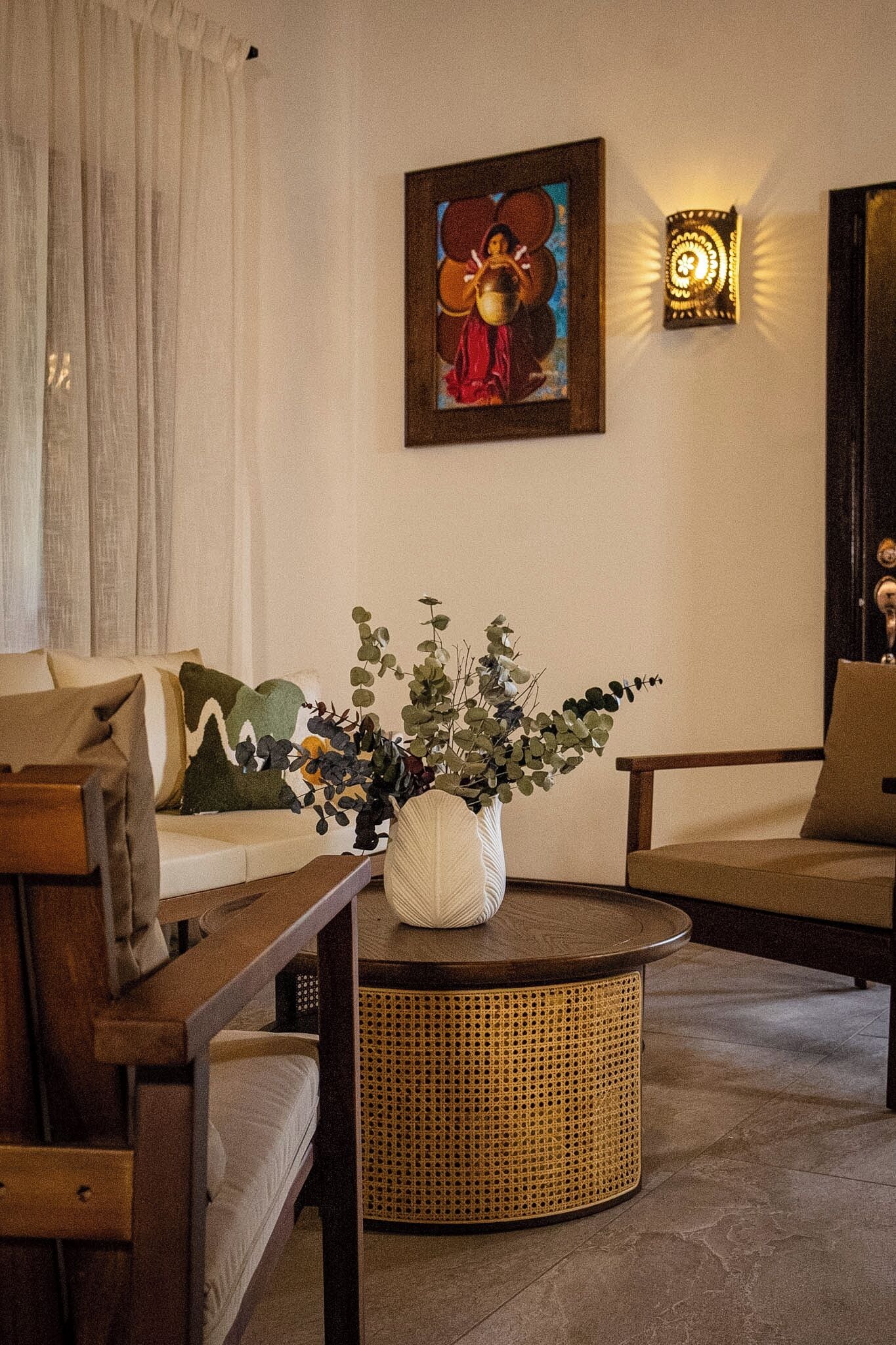 Un salón con una mesa de centro redonda de mimbre, un sofá y un cuadro en la pared.