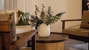 Un salón con una mesa de centro redonda de mimbre, un sofá y un cuadro en la pared.