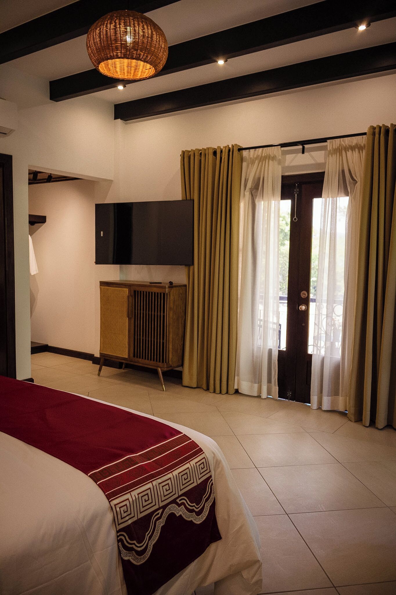 A hotel room with a bed, a television, curtains, and a ceiling light fixture.