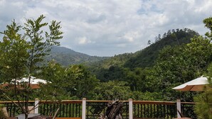 Un patio con una chimenea, rodeado por una valla de madera, con vistas a un paisaje verde exuberante y una montaña.
