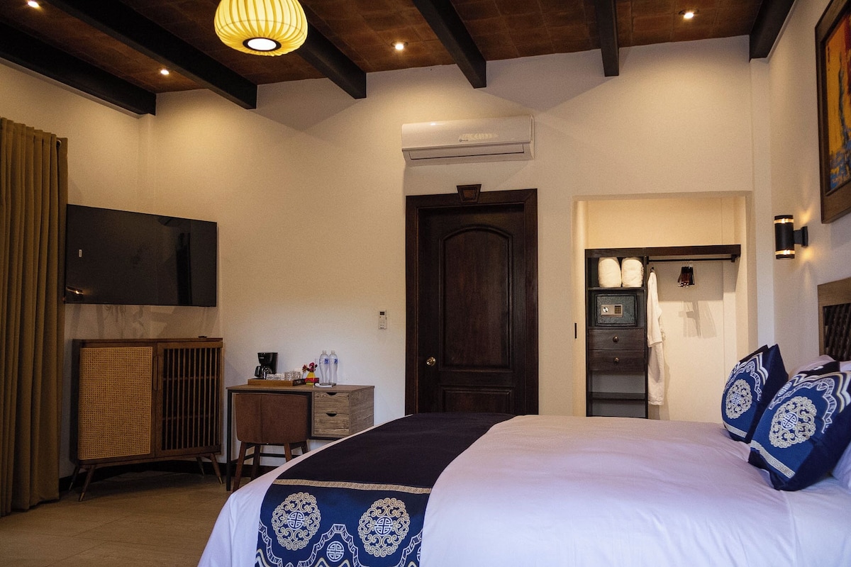 A bedroom with a bed, a desk, a wardrobe, a television, and a door.