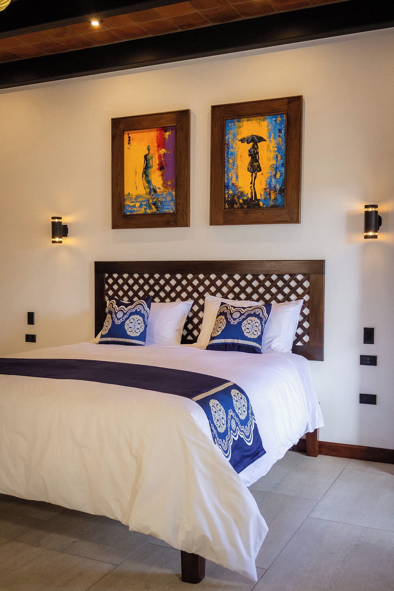 A hotel room with a large bed, two paintings on the wall, and a wooden headboard.