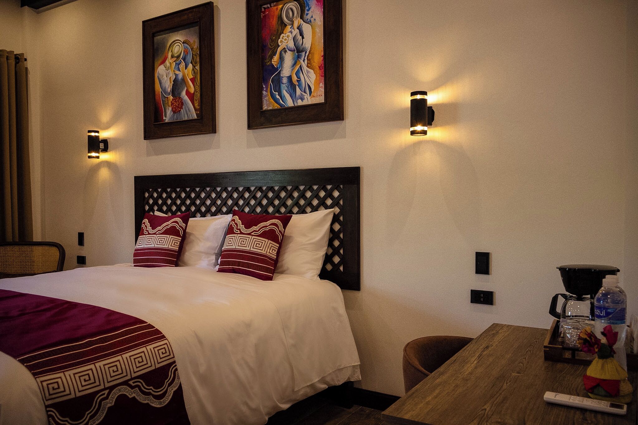 Habitación de hotel con cama, dos lámparas de pared, una cafetera y dos obras de arte enmarcadas.