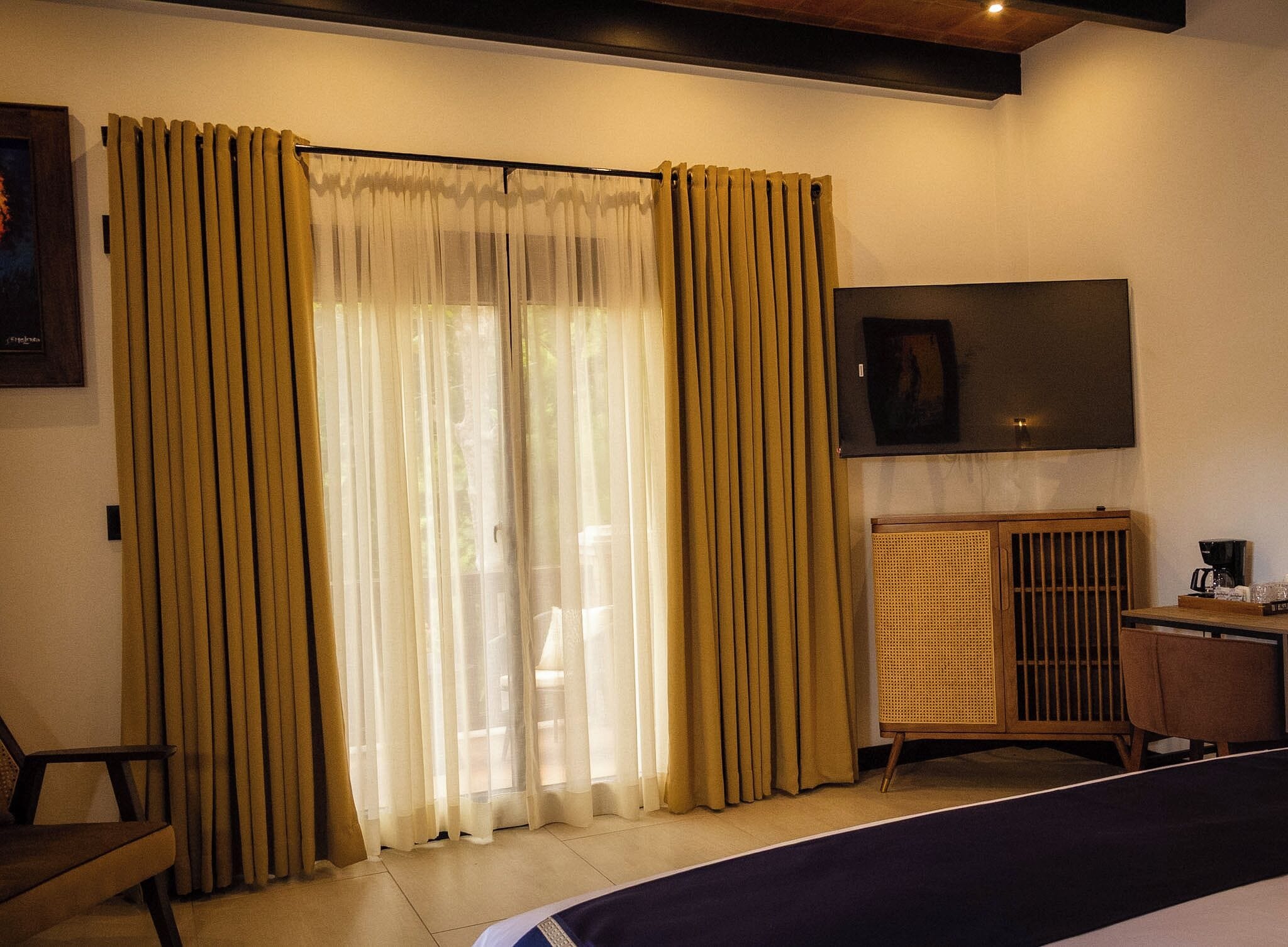 A hotel room with a bed, a desk with a coffee maker, a TV, and curtains.