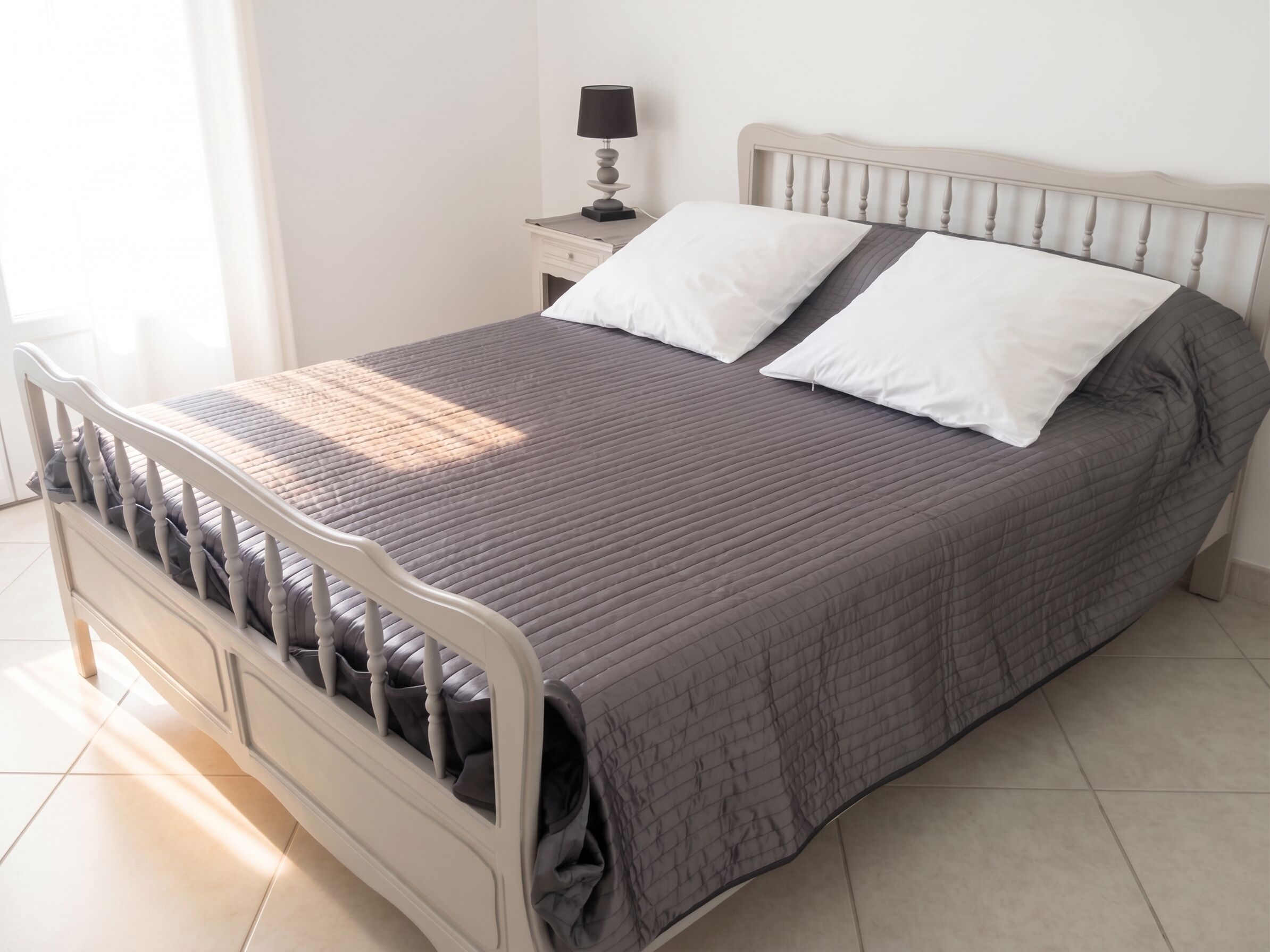 Un lit avec une tête de lit, une table de chevet avec une lampe et une fenêtre avec des rideaux.