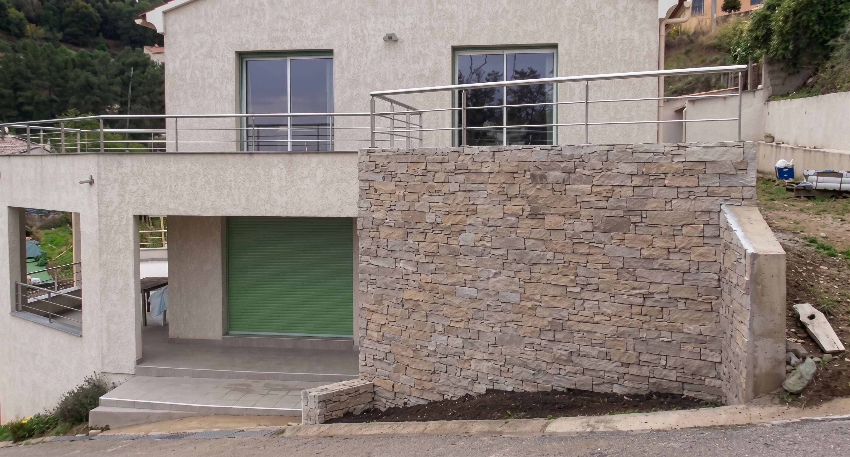 A modern building with a stone facade, a green garage door, and a metal balcony railing.