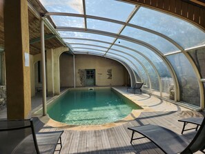 A covered swimming pool with a glass ceiling, wooden deck, and lounge chairs. - Secluded vacation rental with a pool in the heart of the Corbières – Nature & Relaxation (Lairière)