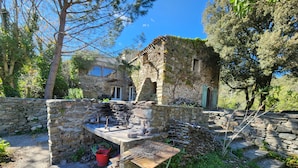 A rustic stone building with a stone wall and a wooden table with metal grill grates. - Secluded vacation rental with a pool in the heart of the Corbières – Nature & Relaxation (Lairière)
