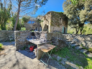 A rustic stone building with a stone wall and a wooden table with metal grill grates. - Secluded vacation rental with a pool in the heart of the Corbières – Nature & Relaxation (Lairière)